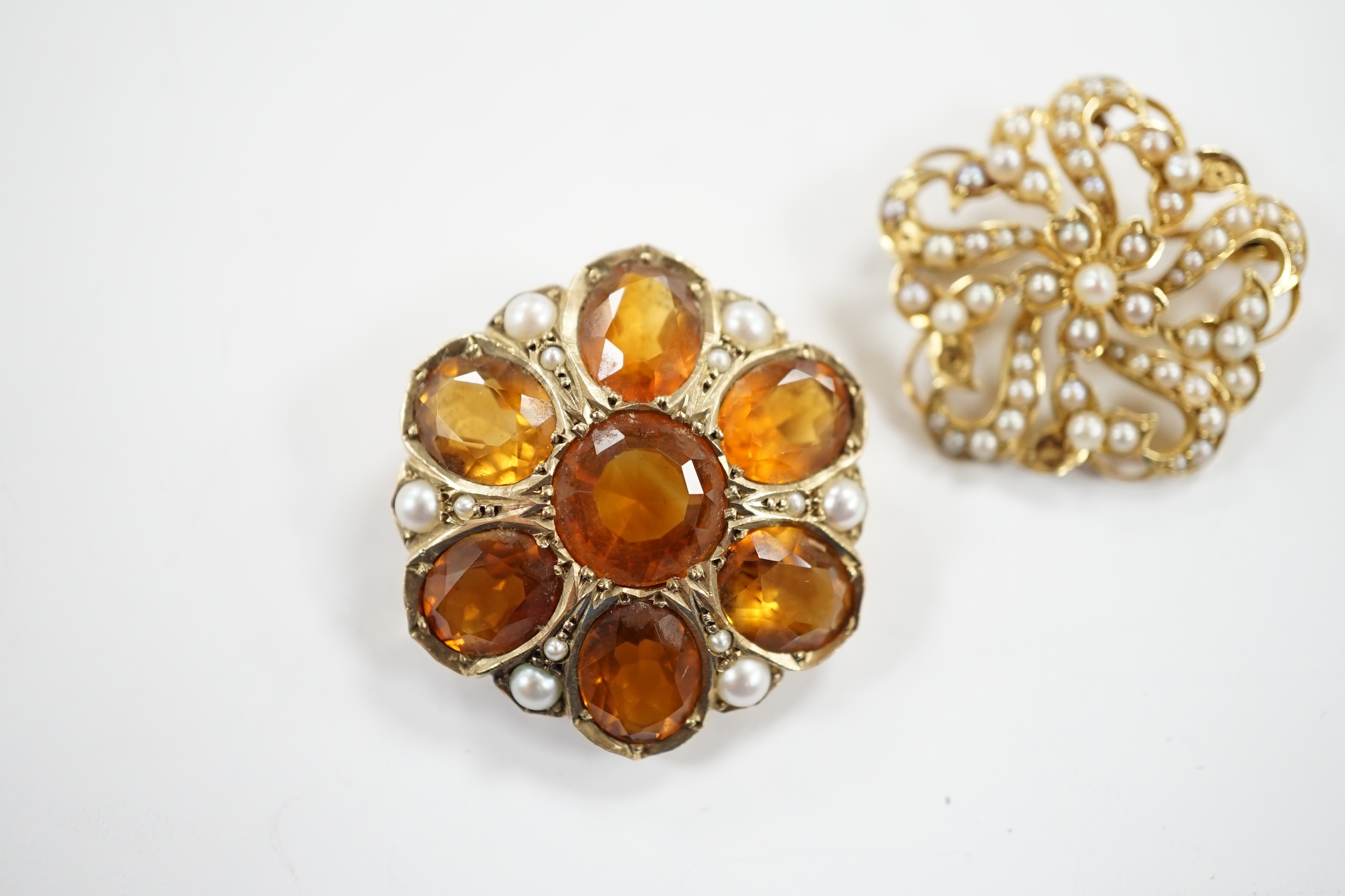 An early 20th century yellow metal, citrine and split pearl cluster set shaped circular brooch, 28mm and a similar 15ct and seed pearl cluster set brooch, gross weight 18.5 grams.